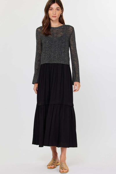 Model wearing a black midi dress with flowy tiered skirt and textured open-knit long sleeve sweater layered over the top.