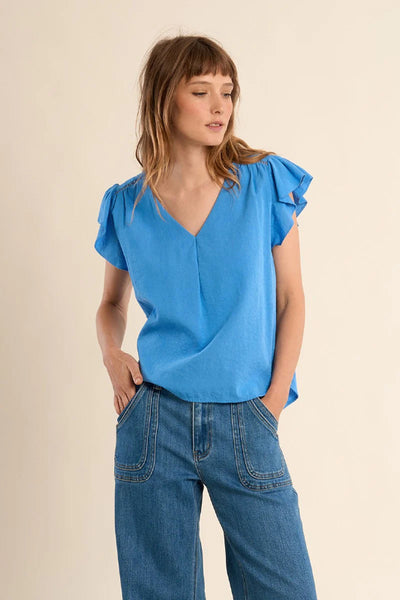 Blue flowing V-neck top with ruffle flutter sleeves and straight fit, styled with wide-leg blue jeans — front view.