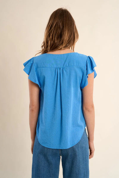 Blue flowing V-neck top with ruffle flutter sleeves and straight fit, styled with wide-leg blue jeans —back view.