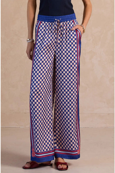 Navy, red, and  ivory geo print wide leg palazzo pants with red striped side panels, elastic drawstring waist, and rose hem detail, front view.