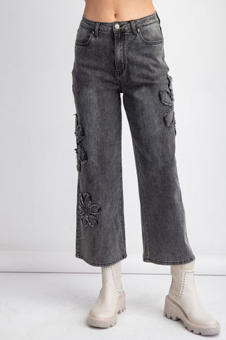 Washed charcoal wide-leg denim jeans with black flower patch detailing, styled with a blush pink oversized top and sneakers.