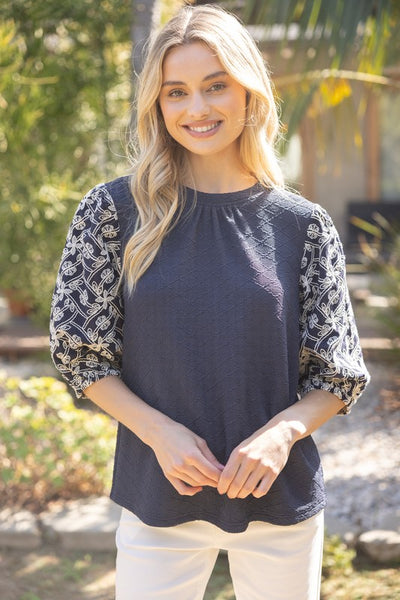 Navy textured knit blouse with embroidered floral sleeves, round neckline, and relaxed fit.