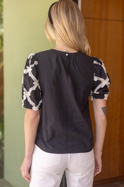 Black puff sleeve top with white bow detail on sleeves.