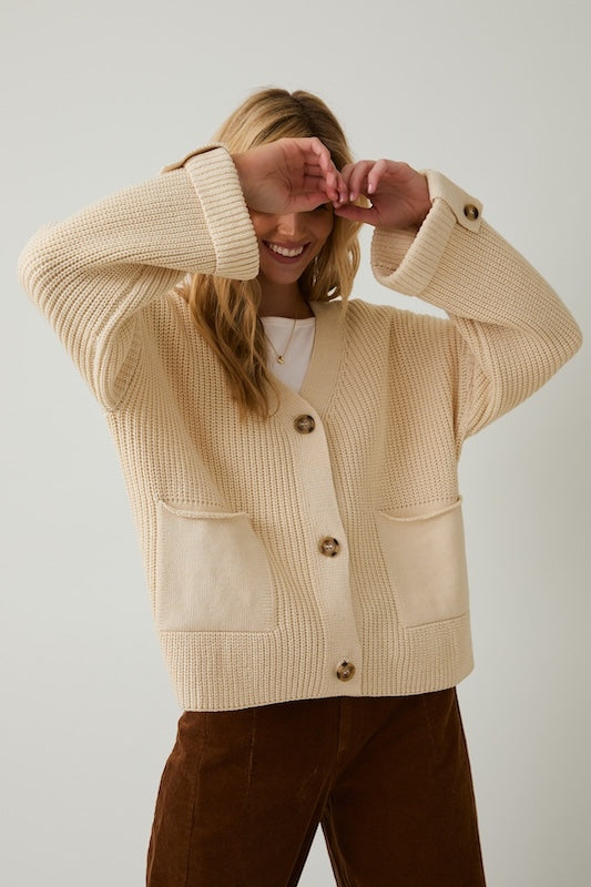 Oversized chunky knit beige cardigan with buttons and front pockets.