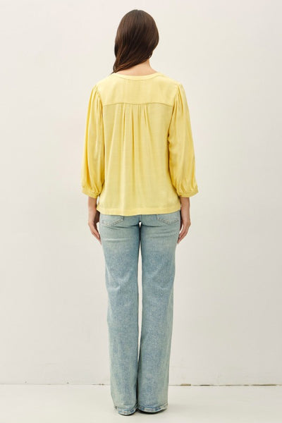 Yellow notched Y-neck volume sleeve top with ruffle cuffs and relaxed fit paired with jeans.