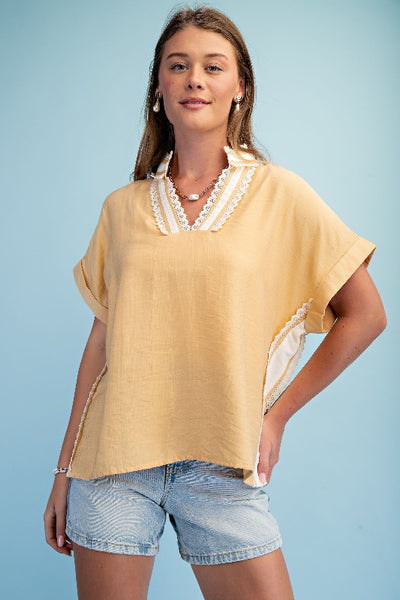 Model is wearing a honey colored V-neck pullover top with white lace-trimmed stripe detail at neckline and rolled cuff short sleeves, front view