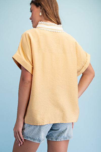 Model is wearing a honey colored  pullover top with white lace-trimmed stripe detail at neckline and rolled cuff short sleeves, back view.