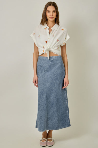 Bias cut denim midi skirt in dark wash with diagonal seam detail and fit-and-flare silhouette, styled with embroidered tie-front shirt.