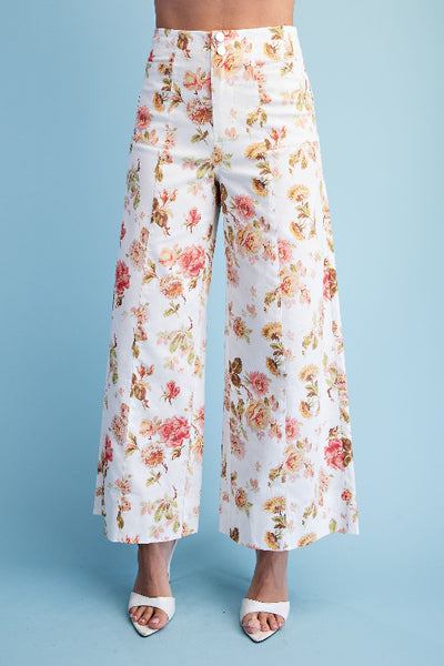 Model is wearing floral print wide leg pants in ivory with pink and yellow rose print, double button closure and seam details, front view. 