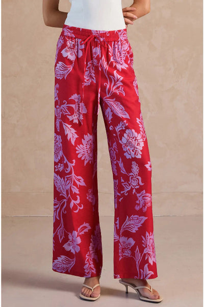 Red wide leg pants with oversized lavender and pink floral digital print, elastic self-tie drawstring waist and side pockets, front view.