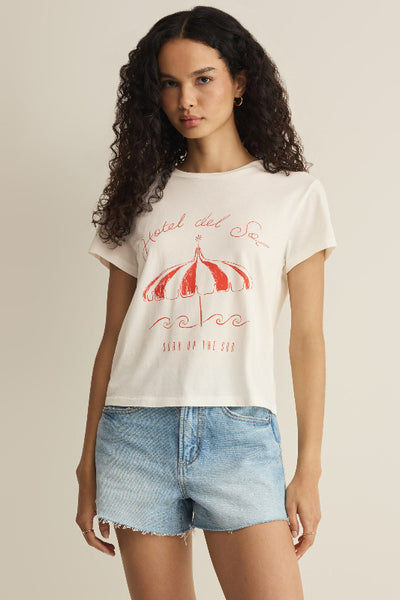 Off-white with a coral red Hotel del Sol beach umbrella graphic, front view on model styled with denim cutoff shorts


