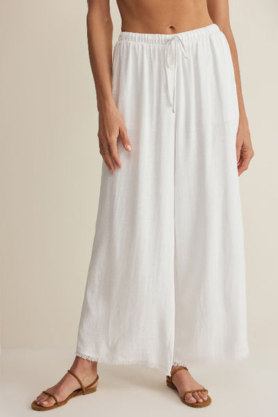 Z Supply Soren Pant in white, a high-rise wide-leg rayon-linen blend pant with tie drawcord and raw frayed hem, styled with tan strappy sandals — front view