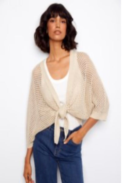 Beige knitted cardigan over a white top and blue jeans on a plain background.