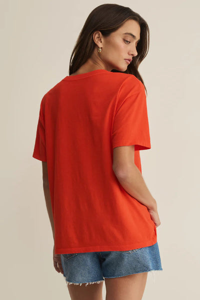 Model is wearing an orange t-shirt and denim shorts on a beige background. Back view of the shirt. 
