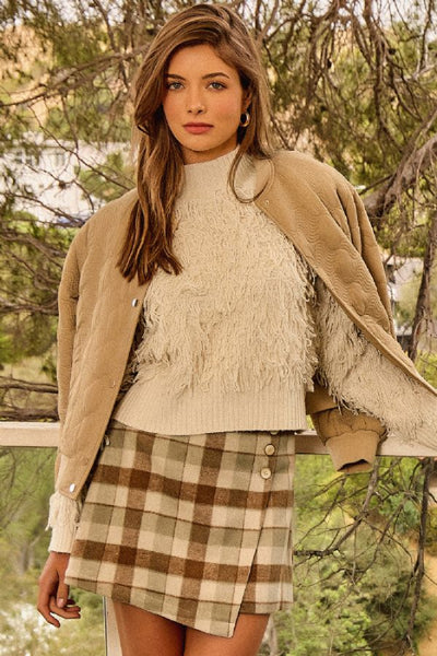 Model wearing a Mystree ivory shaggy knit mock neck sweater with a camel jacket and brown plaid skirt outdoors. Mystree ivory sweater; Mystree shaggy knit sweater; ivory mock neck sweater; women's shaggy pullover sweater; textured ivory sweater; long sleeve mock neck sweater; ivory fall sweater for women; women's neutral winter sweater; Mystree 61640 sweater; ivory sweater with ribbed hem