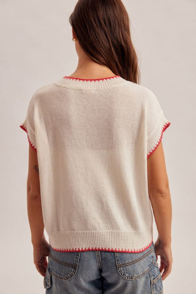 Cream lightweight knit sweater top with an American flag intarsia graphic on the front and red contrast stitching at neckline and sleeves, styled with denim shorts, back view.
