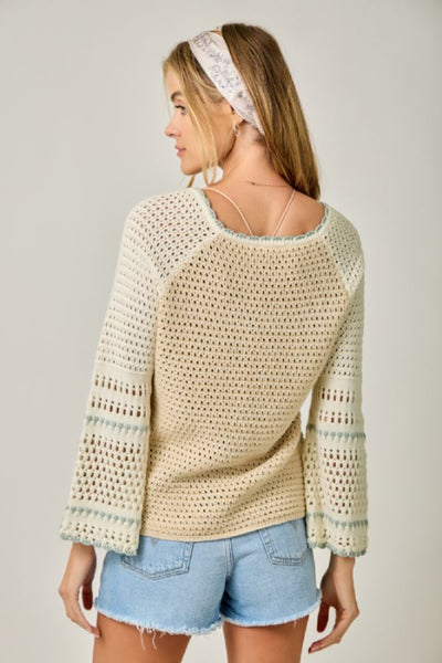 Raglan Sleeve Crochet Sweater in oatmeal, back view, open-crochet pattern, bell sleeves with striped detail, and loose fit with denim shorts