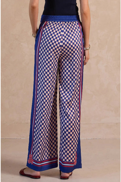 Navy, red, and  ivory geo print wide leg palazzo pants with red striped side panels, elastic drawstring waist, and rose hem detail, back view.