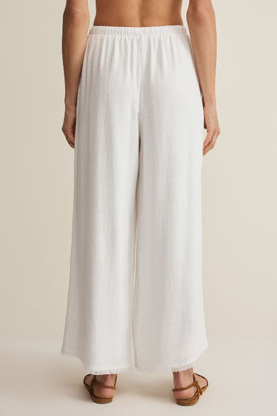 Z Supply Soren Pant in white showing the back view with elasticated waistband and raw frayed hem, styled with tan strappy sandals — back view