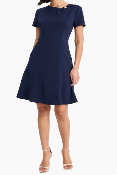 Maggy London navy short sleeve fit and flare dress with goldtone brooch at gathered crewneck, front view