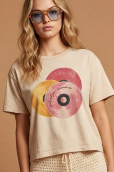 Model is wearing the  Girl Put Your Records On Tee in sand beige with a retro vinyl record graphic, styled with high-rise shorts.