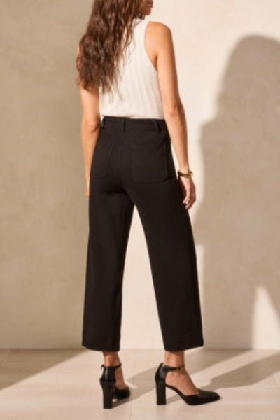 Black high-rise ponte capri pants with pockets, styled with white sleeveless top and black heels — back view.