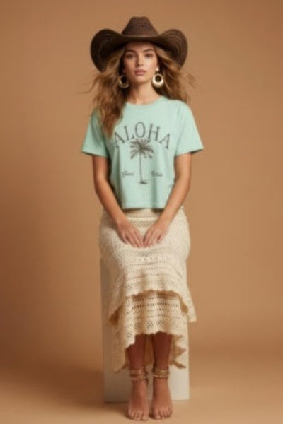 Model is wearing Aloha Wide Boy Tee in mint green with a palm tree graphic, styled with a crochet midi skirt and cowboy hat.