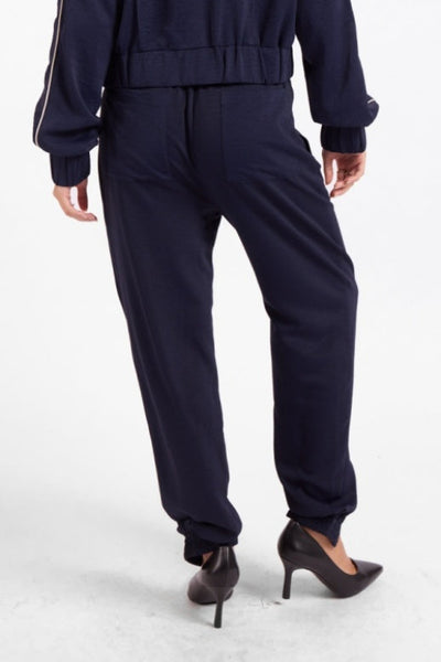 Back view of Sage the Label navy joggers with patch pockets and elastic cuffs;Sage the Label Bike Ride Joggers
Sage the Label navy joggers
women’s navy and ivory joggers
navy joggers with ivory piping
women’s tapered jogger pants
women’s pull-on track pants
women’s matching track set
lined polyester joggers for women
sporty chic navy pants
relaxed-fit ankle joggers