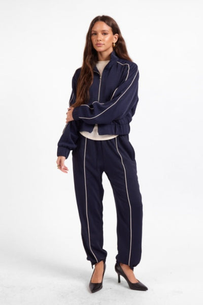 Model wearing Sage the Label Bike Ride navy track jacket and matching joggers.Sage the Label Bike Ride Track Jacket
Sage the Label navy track jacket
women’s navy and ivory track jacket
women’s cropped track jacket
navy jacket with ivory piping
sporty chic jacket for women
women’s matching track set
relaxed fit zip-front jacket
women’s boutique athleisure jacket
navy cropped lightweight jacket