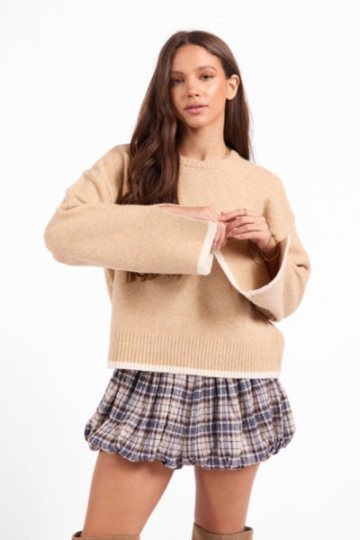 Sage the Label Angelina Cuff Slit Crew Neck Sweater in beige ivory, relaxed oversized fit, wide long sleeves with cuff slit detail, ribbed hem, styled with a plaid bubble mini skirt — front view