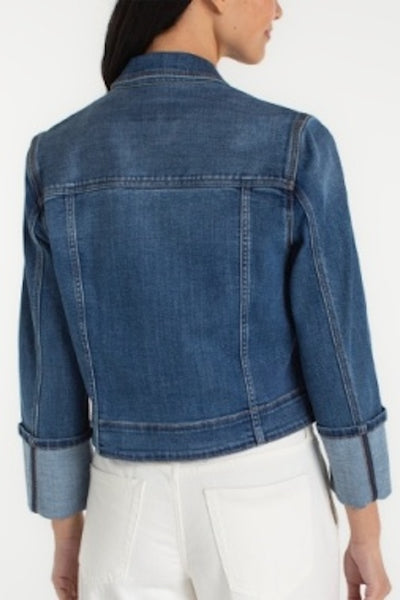 Back view- Medium blue cropped denim trucker jacket with wide cuffed bracelet-length sleeves and button-front closure, styled with white pants.